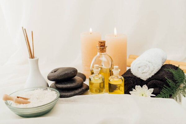 close up view of arrangement of spa treatment accessories with towels, pebbles and essential oil on white background