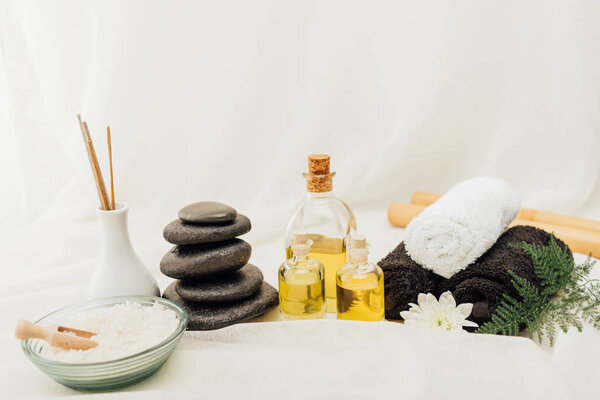close up view of arrangement of spa treatment accessories with towels, pebbles and essential oil on white background