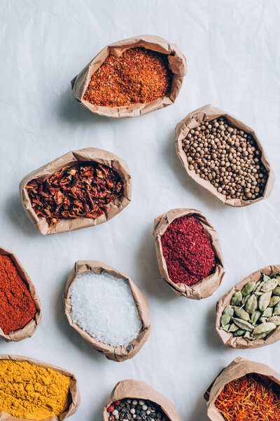 top view of colorful indian spices in paper bags on white table
