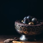 Closeup view of dry orange slices, candies in vintage bowl and chocolate pieces on black background