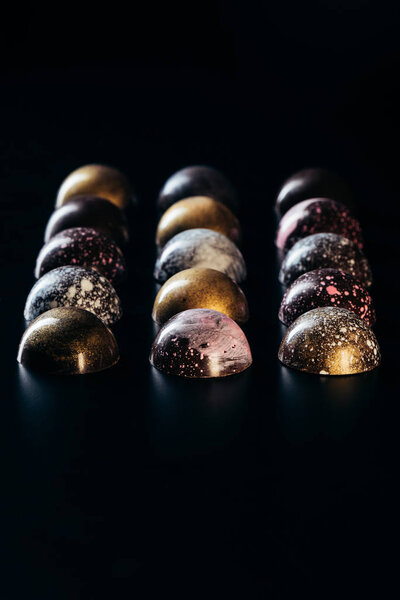 different chocolate candies placed in rows on black background 