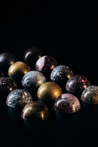 various chocolate candies placed in rows on black background 