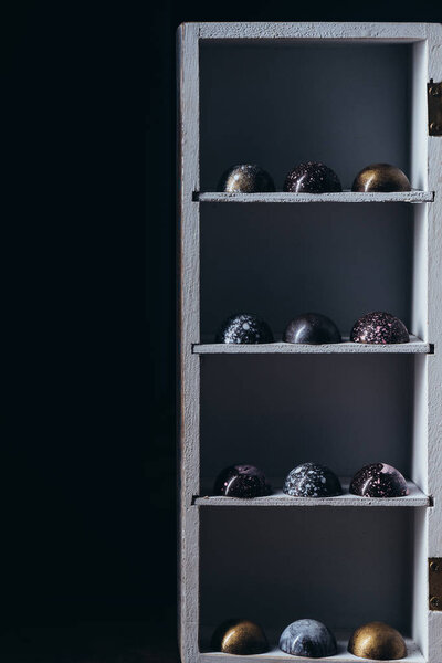 various chocolate candies placed in rows on shelves on black background