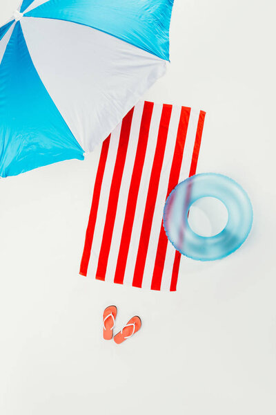 top view of beach umbrella, striped beach towel, flip flops and inflatable ring isolated on white