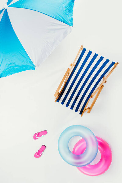 top view of beach umbrella, striped beach chair, flip flops and inflatable rings isolated on white