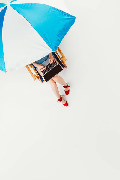 top view of girl sitting in beach chair and using laptop isolated on white