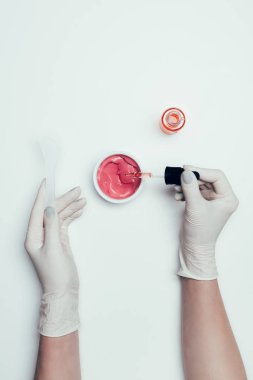 Lateks eldiven kaşık ve boru konteyner yakınındaki beyaz yüzey üzerinde izole pembe maske ile tutan kadının kırpılmış görüntü