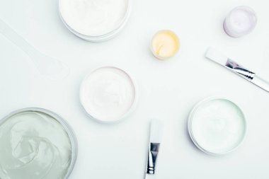 düz lay farklı kil maskeleri kapsayıcılar ve beyaz yüzey üzerinde izole fırçaları ile 