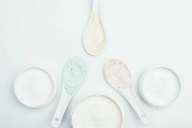 Konteyner ve kaşık beyaz yüzey üzerinde izole çeşitli renkli kil maskeleriyle düz lay 