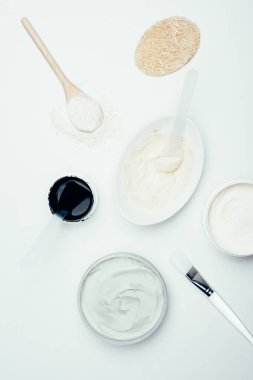 düz lay sünger, kapsayıcılar, kil tozu, kaşık, tabak ve beyaz yüzey üzerinde izole fırça içinde çeşitli kil maskesi ile 