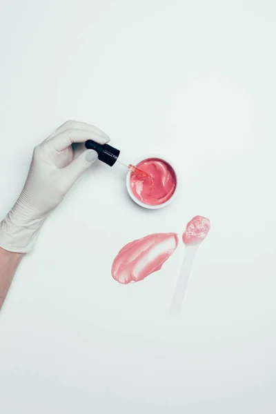 一只手在乳胶手套管附近的容器与粉红色的面具 勺子和污迹在白色表面 — 免费的图库照片