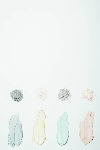 flat lay with different clay powder and colorful clay mask smudges placed in row isolated on white surface 