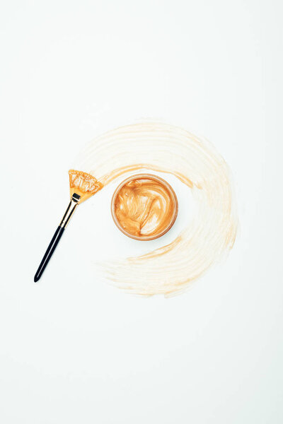 вид сверху на золотую маску в контейнере, окруженный пятном с кистью, изолированной на белой поверхности
 