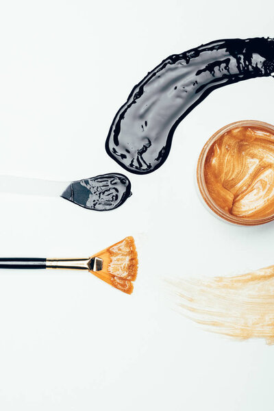 flat lay with black and golden masks, brush and spoon isolated on white surface 