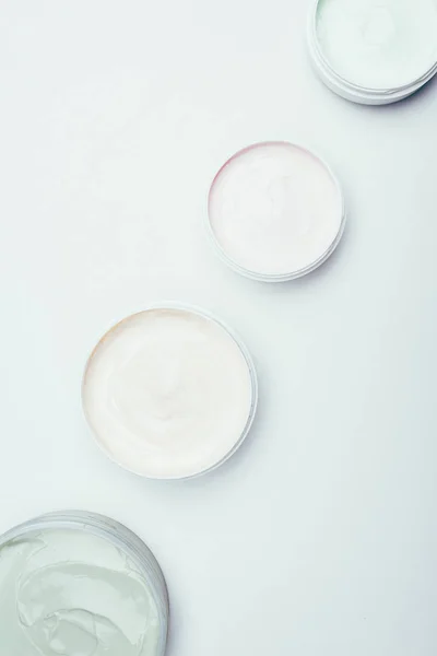 flat lay with different clay masks in containers placed in row isolated on white surface