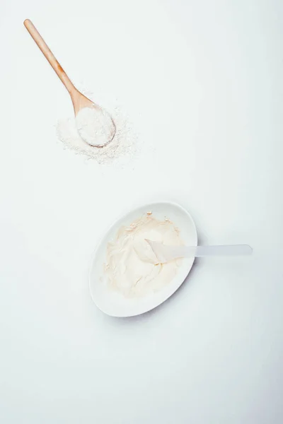 top view of spoons, clay powder and plate with clay mask isolated on white surface