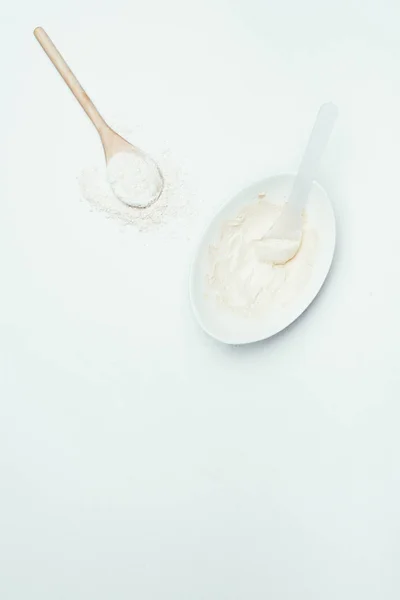 top view of spoons, clay powder and plate with clay mask isolated on white surface