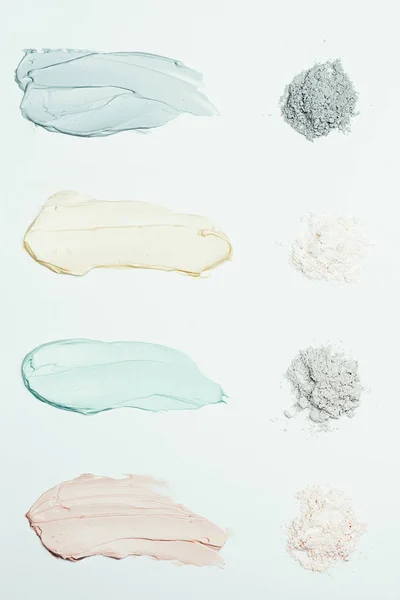 flat lay with clay powder and four colorful clay mask smudges placed in row isolated on white surface