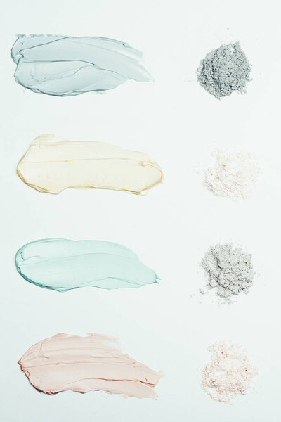 flat lay with clay powder and four colorful clay mask smudges placed in row isolated on white surface 