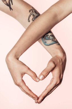 kısmi görünümü ellerinizle, pembe arka plan izole kalp sembolü yapan dövmeli erkek ve kadın 