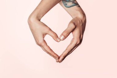 Kırpılan atış ellerinizle, pembe arka plan izole kalp sembolü yapan dövmeli erkek ve kadın 