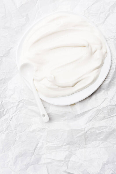 top view of sour cream on plate with spoon on white crumpled paper