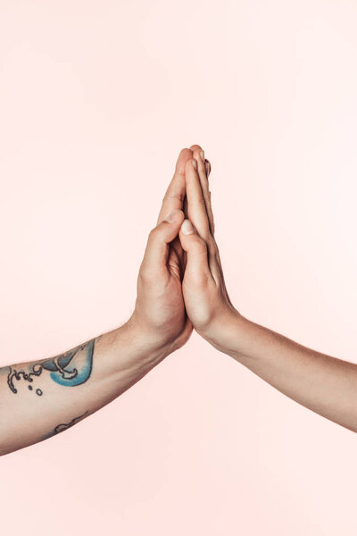 cropped shot of tattooed man and woman holding palms together isolated on pink background 