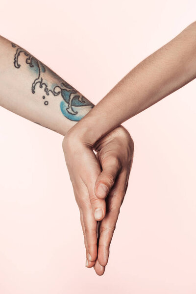 partial view of tattooed man and man holding palms together isolated on pink background 