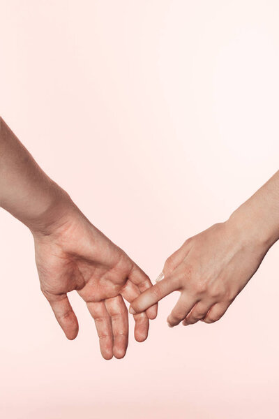 cropped shot of woman holding man hand by finger isolated on pink background 