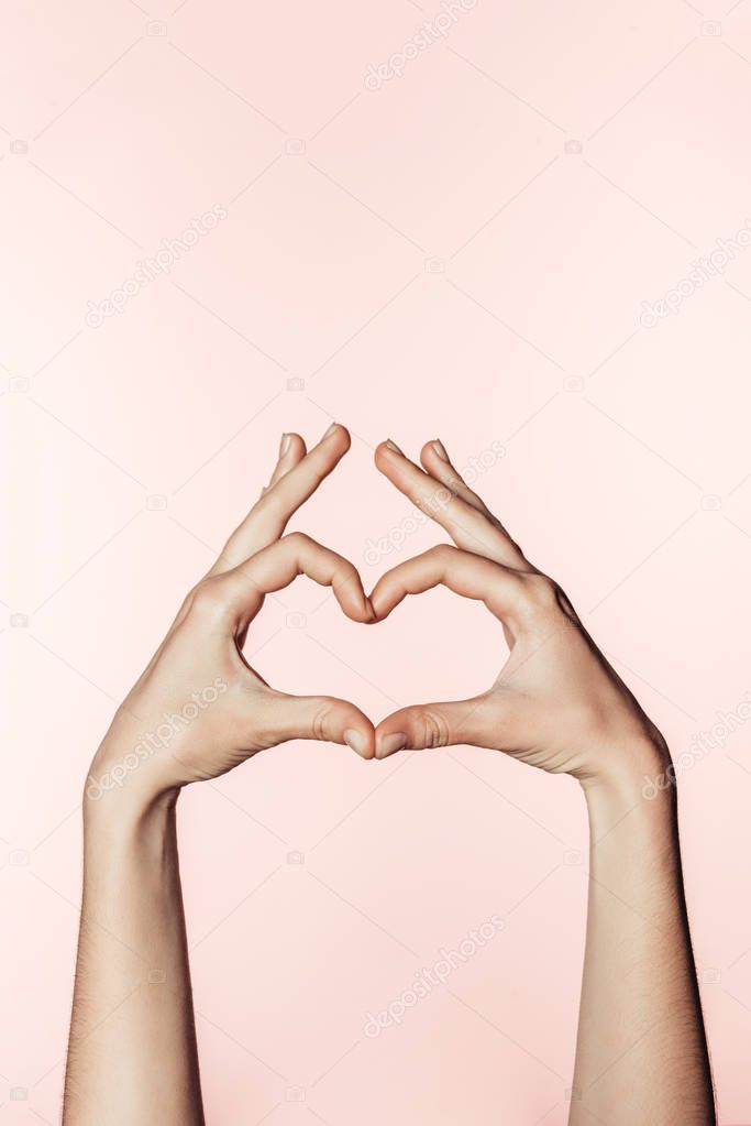 partial view of woman doing heart symbol by fingers isolated on pink background 