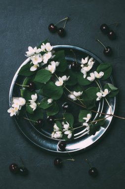 top view of beautiful white jasmine flowers and ripe sweet cherries on black  clipart