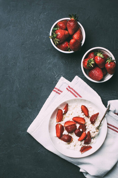 top view of healthy cottage cheese and fresh ripe strawberries in bowls on black 