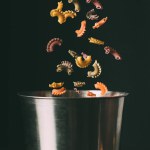 Närbild skott av färgglada pasta falla i pan på svart bakgrund