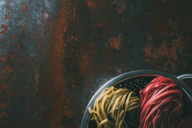 rustik metal masa üzerinde yeşil ve kırmızı tagliatelle makarna kevgir içinde üstten görünüm