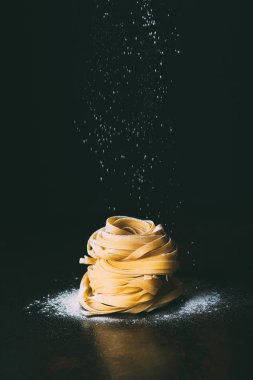 closeup shot of flour falling on tagliatelle pasta on black background  clipart