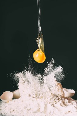 close up view of yolk falling on flour on black background  clipart