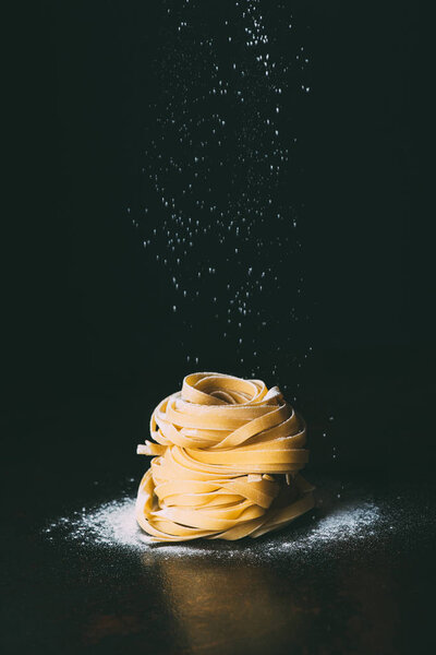 closeup shot of flour falling on tagliatelle pasta on black background 