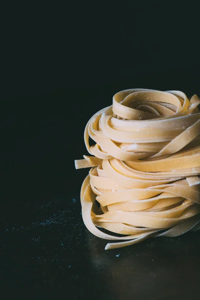 close up image of raw tagliatelle pasta covered by flour on black background 