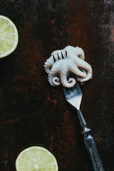top view of little octopus on fork on rusty metal surface with limes