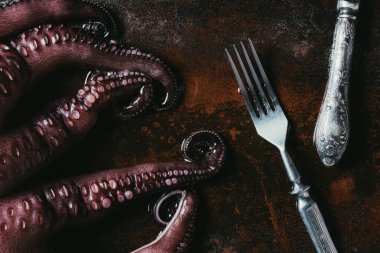 top view of big octopus with fork and knife on rusty metal surface clipart