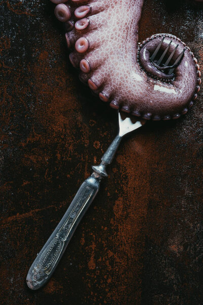 top view of big octopus tentacle with fork on rusty metal surface