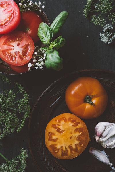 top view of red and yellow tomatoes with flowers, garlic and basil leaves
