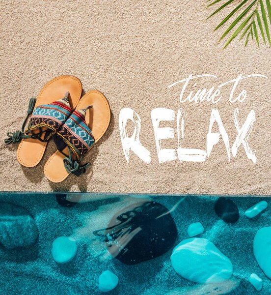 top view of stylish flip flops on sandy beach with "time to relax" inspection