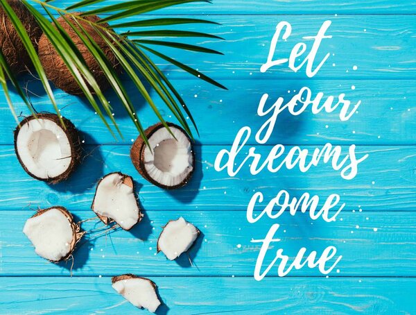 top view of coconuts and green palm leaves on turquoise wooden surface with "let your dreams come true" lettering 