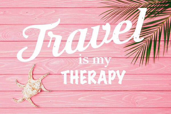 верхний вид ракушки с пальмовыми листьями на розовой деревянной поверхности с надписью "Путешествие это моя терапия"
 