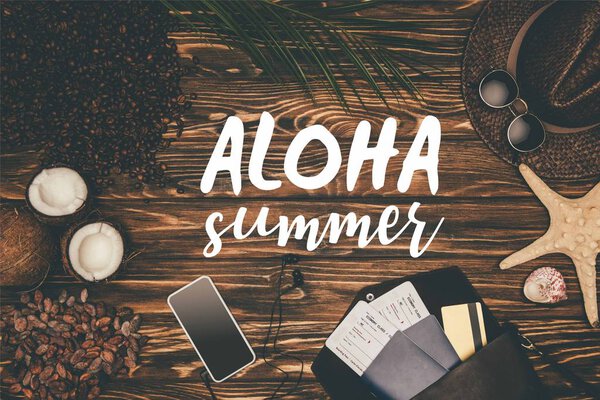 top view smartphone and flight tickets surrounded with various tropical travel attributes on wooden surface with "Aloha summer" lettering 