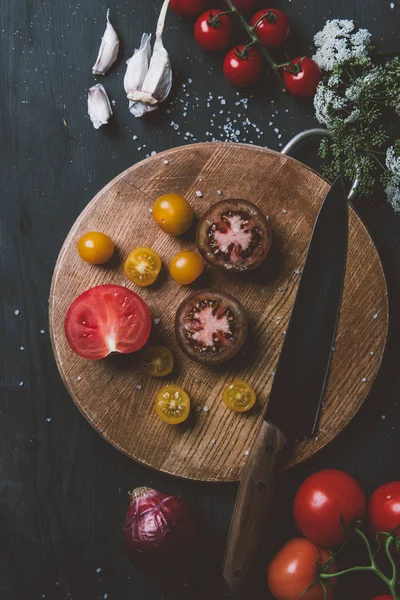 Top view of black prince tomatoes and yellow cherry tomatoes on wooden cutting board with knife, garlic, salt and flowers — Stock Image Top View Black Prince Tomatoes Yellow Cherry Tomatoes Wooden Cutting Stock Image