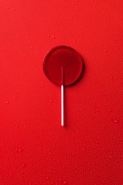 top view of one lollipop on red surface with water drops clipart