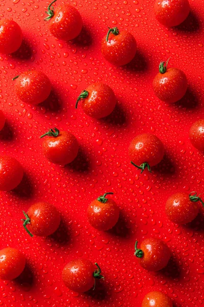 top view of pattern of cherry tomatoes on red surface with water drops