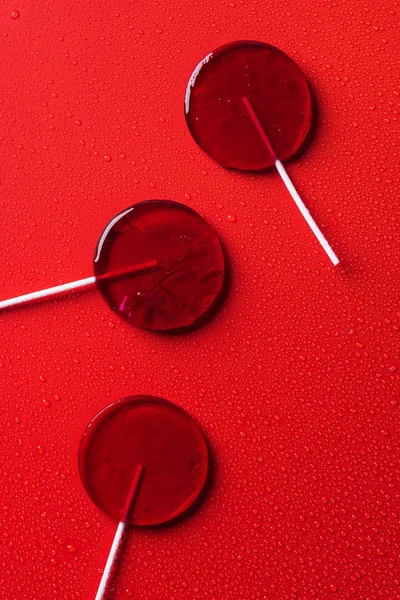 Vista Superior Tres Piruletas Superficie Roja Con Gotas Agua —  Fotos de Stock